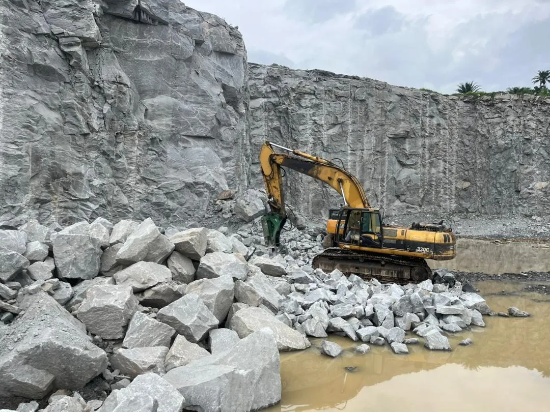 Excavator with a hydraulic breaker extracting granite at the Okeigbo Quarry rock face